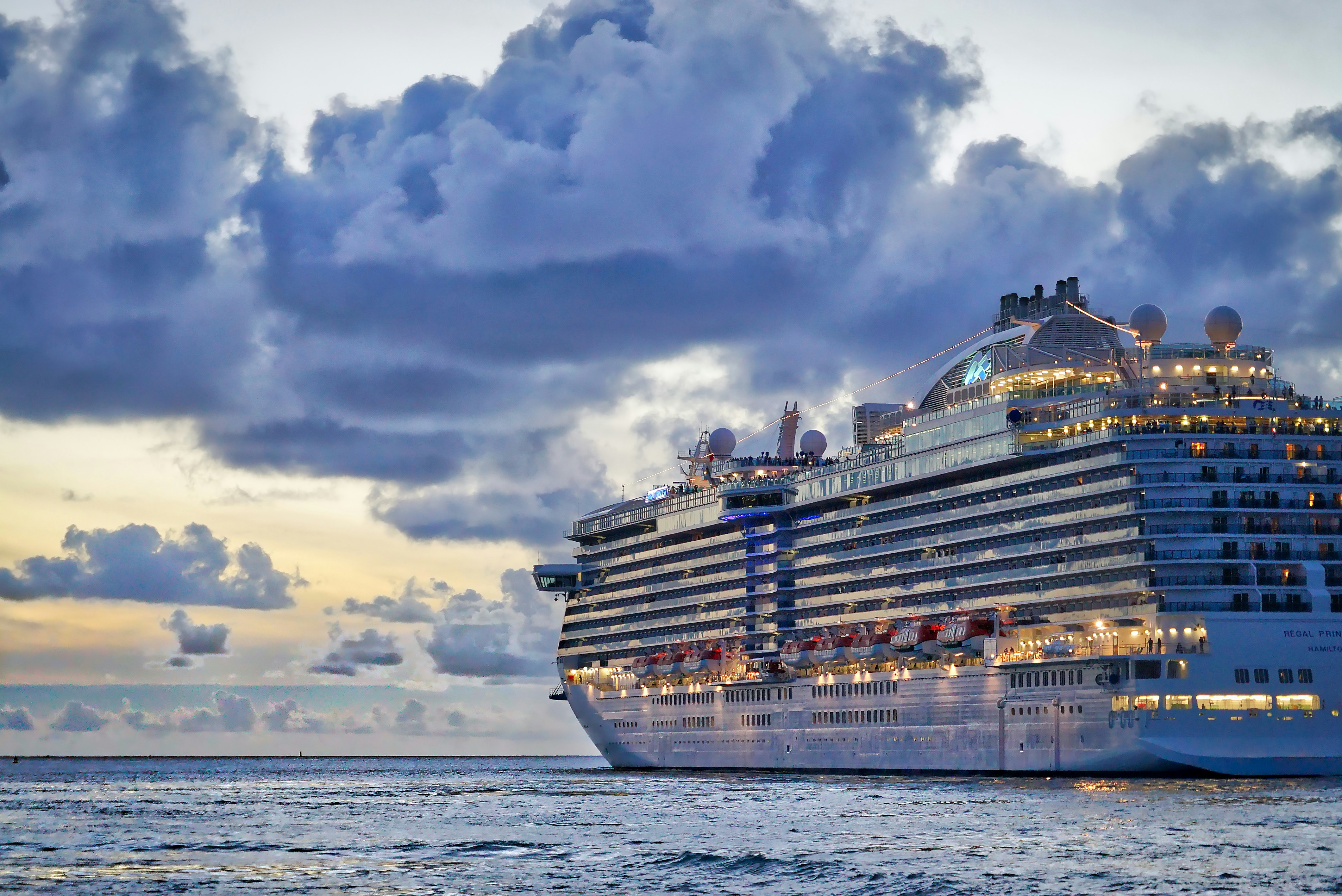 Large cruise ship departing a UK port at sunset under dramatic clouds, cabin lights glowing across her decks