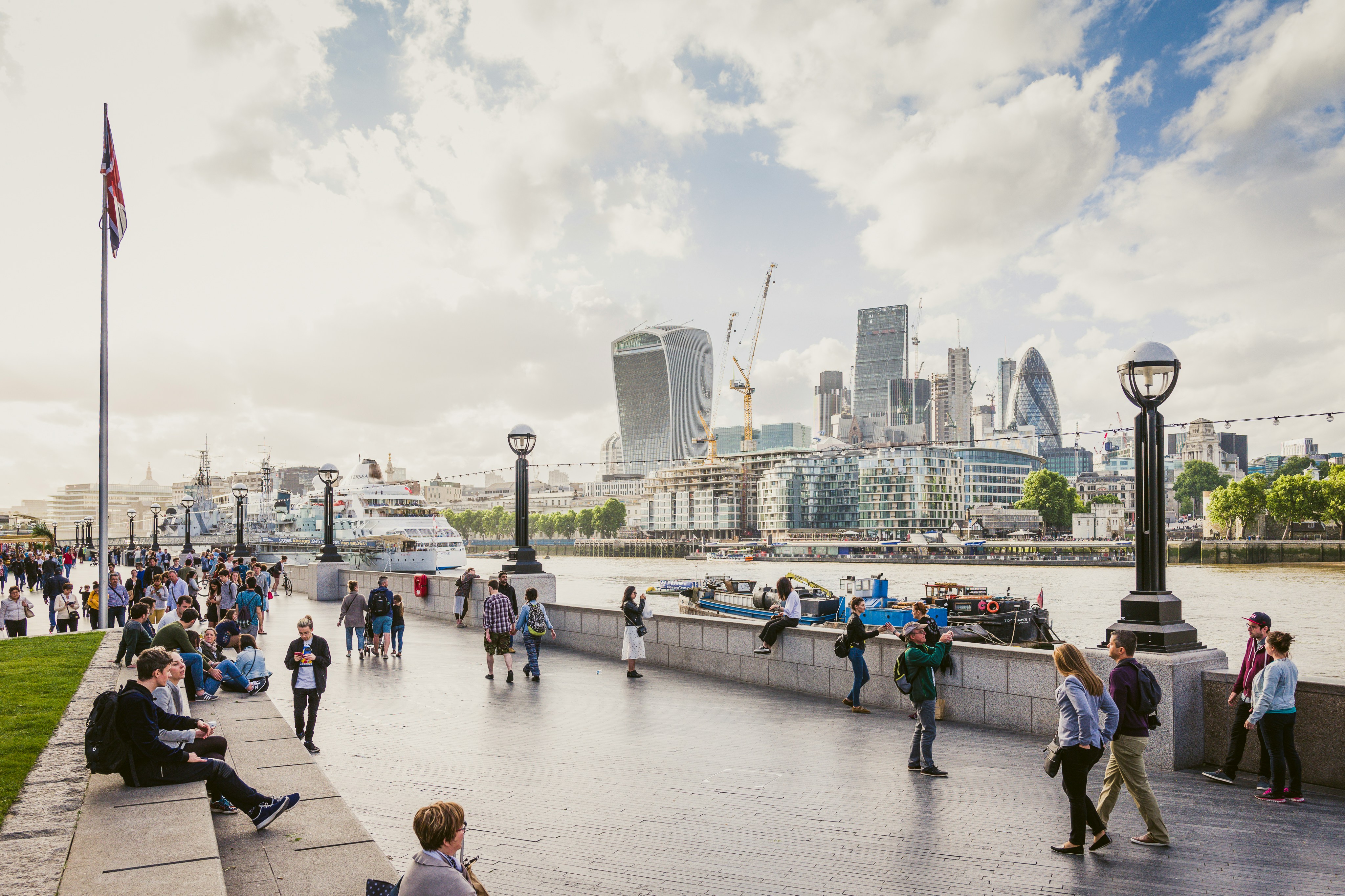 Travellers walking the Thames riverside promenade with the City of London skyline beyond — the calm pre-cruise morning this guide's timing strategy is designed to protect